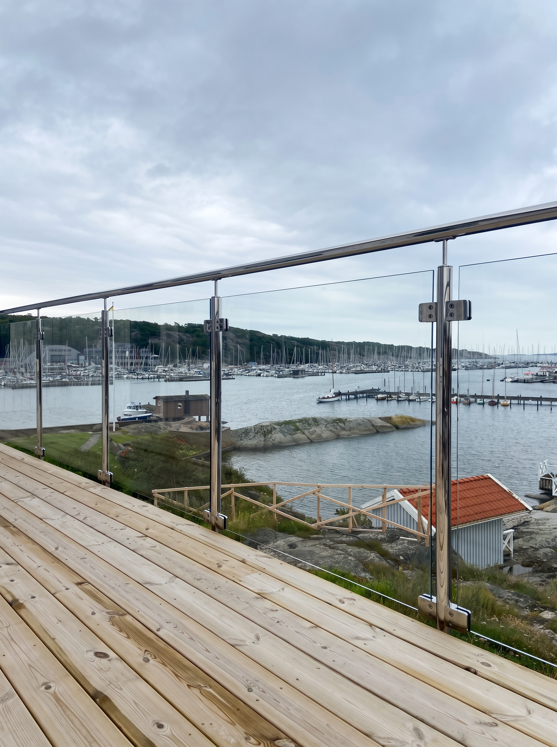 Sidomonterat glasräcke med högblankpolerade rostfria stolpar och utsikt över småbåtshamn